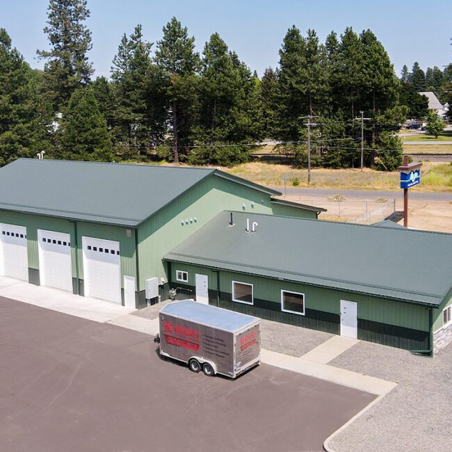 aerial view of a green commercial steel structure building with gray roof and 4 white overhead garage doors