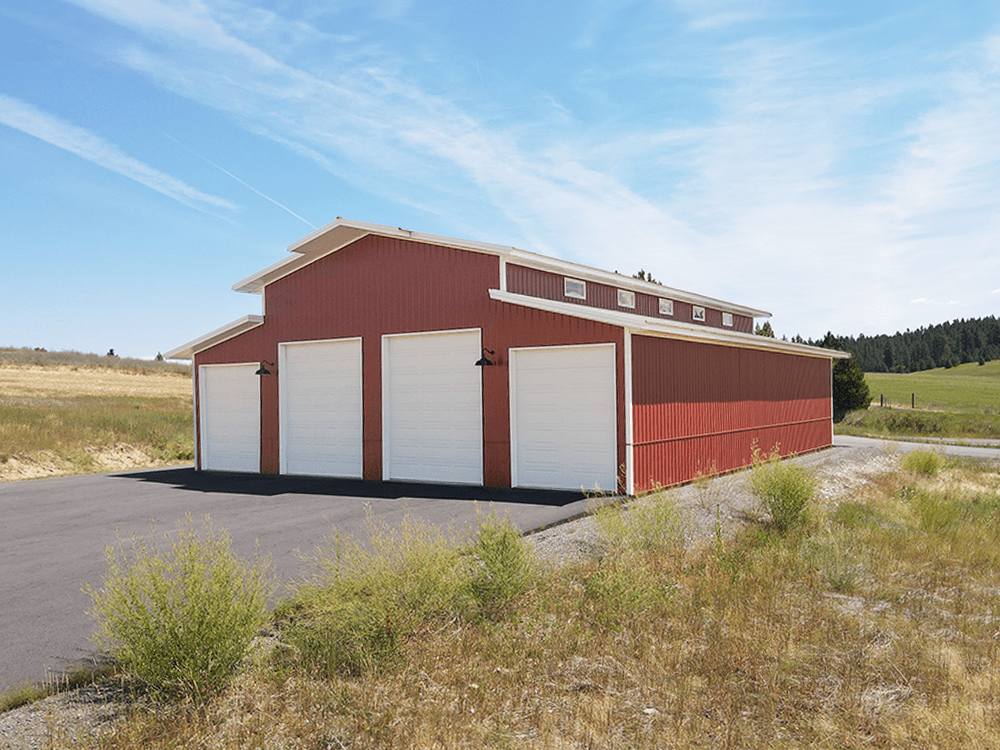 Red steel structure barn with white trim and 4 white over-head garage doors