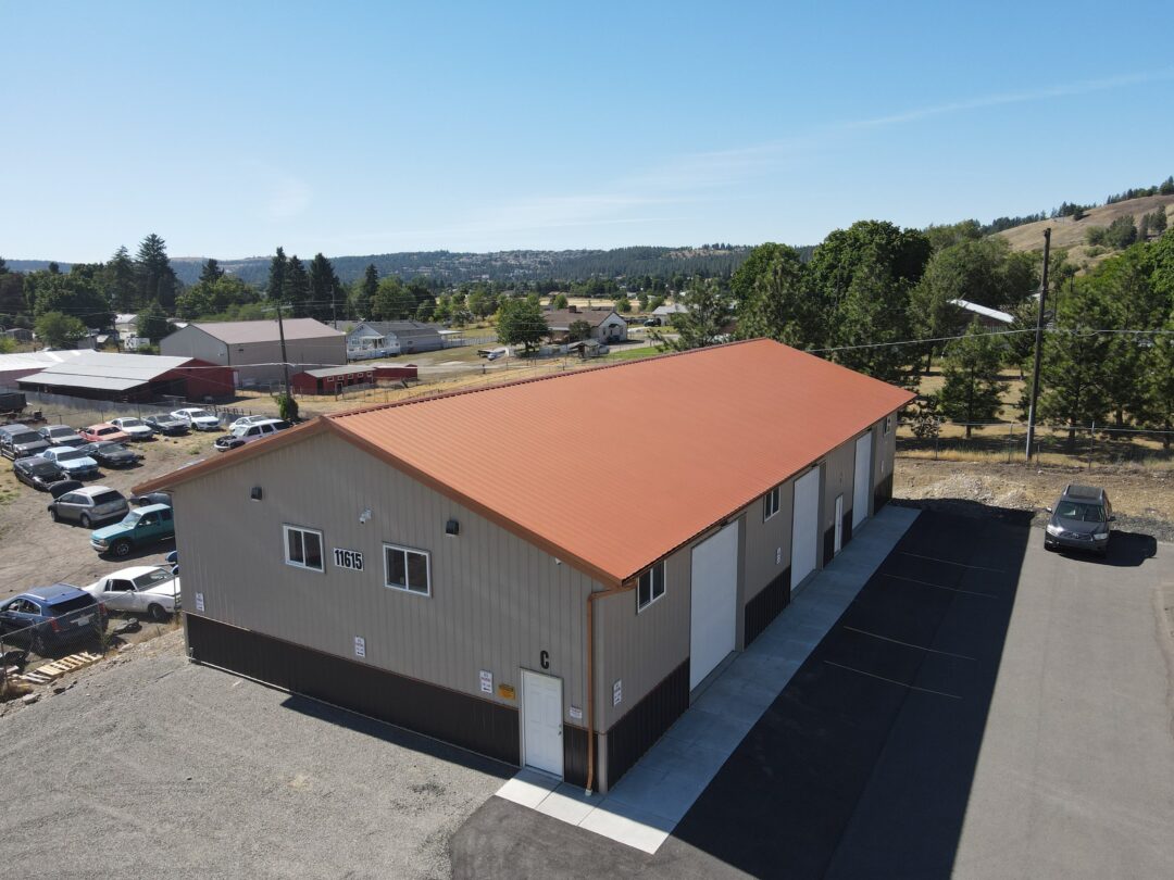 aerial view of steel structure commercial building with red roof and beige siding and white overhead garage doors