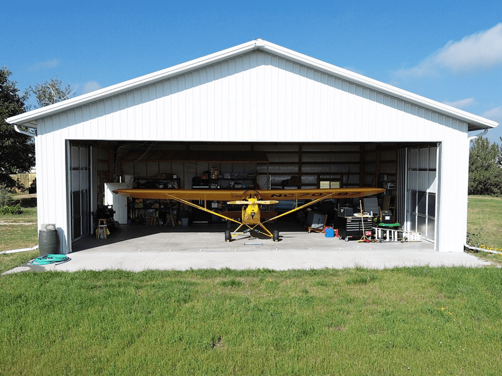 yellow airplane parked inside of a white stell structure pole hanger