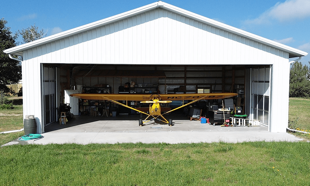 yellow airplane parked inside of a white stell structure pole hanger