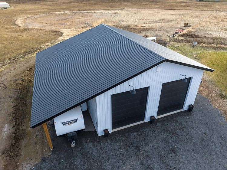 An RV or camper trailer is parked under the lean-to of a shop building