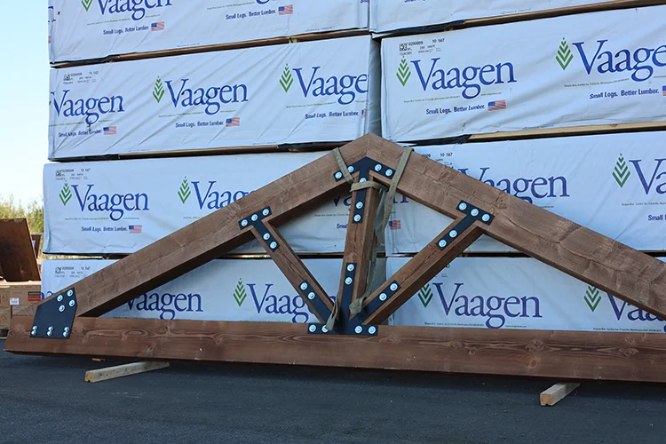 A roof truss for a post frame building leans against stacks of lumber