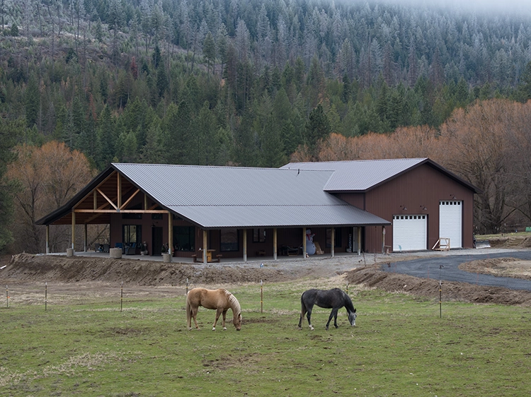 Two horses are grazing outside of a custom horse barn and pole building