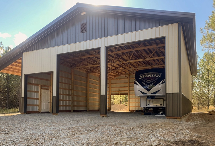 A shop with large overhead doors open has a large RV inside