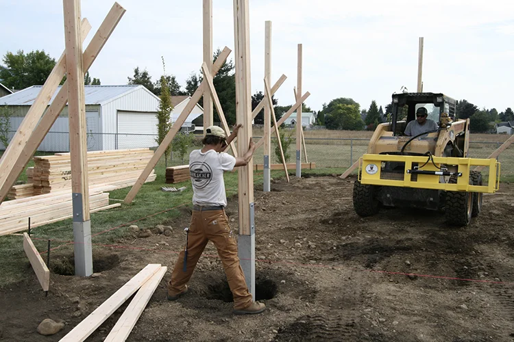 A crew sets perma-column posts after prepping the site foundation for a post frame pole barn