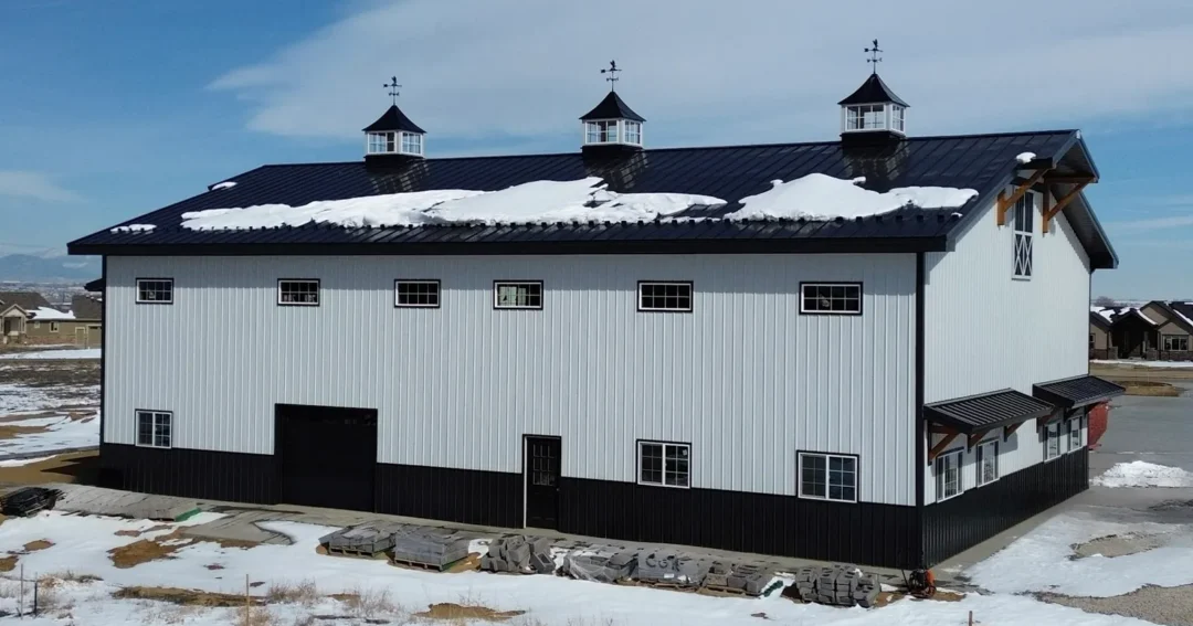 A white two story pole barn with a black roof and trim