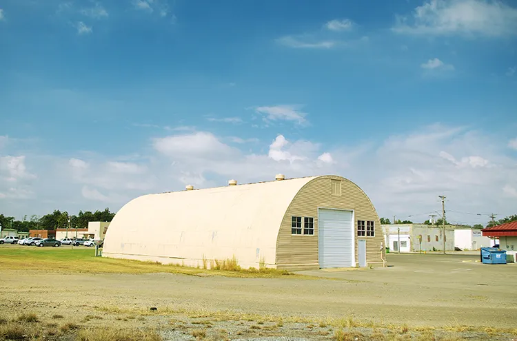 An old yellow quonset hut sits in a field